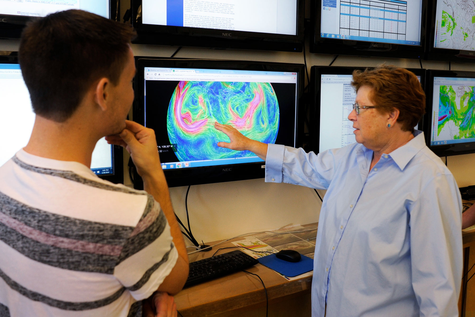 A professor points to a screen showing weather patterns to a student.