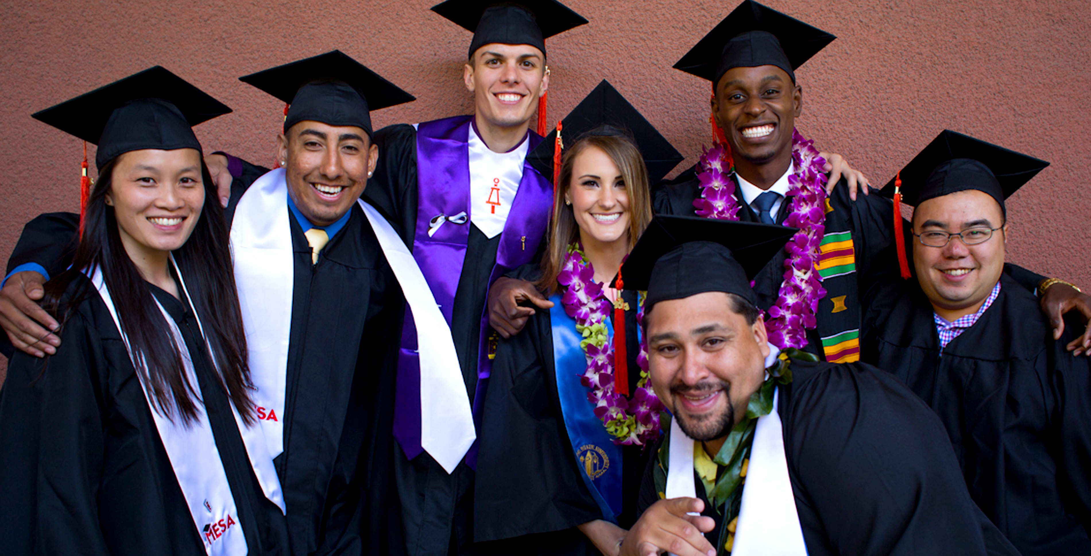 SJSU graduates in cap and gowns embracing.