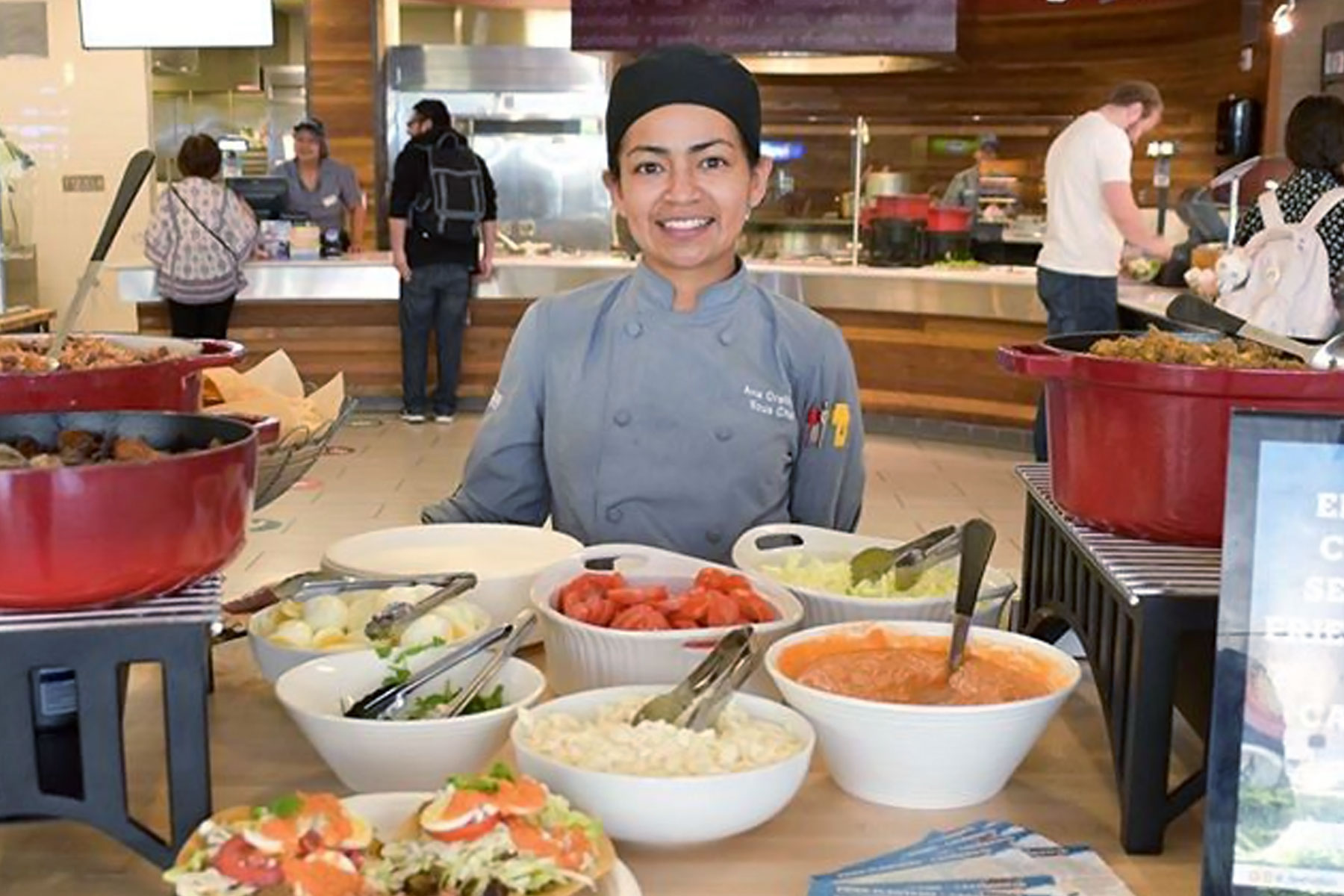 Female server behind a table of food options.