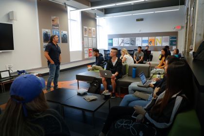 Speaker standing before students sitting on couches with laptops