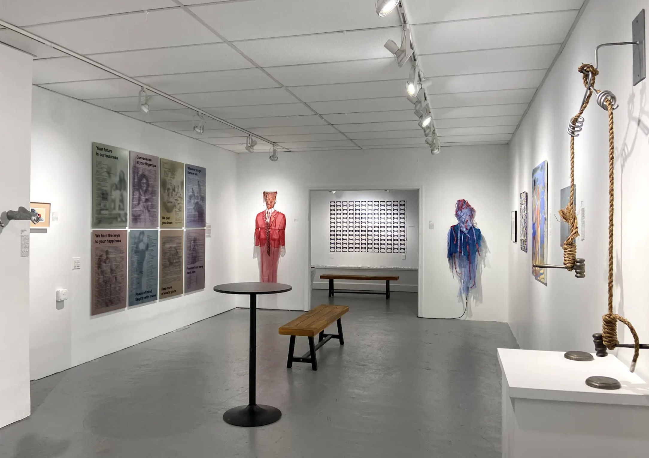 Gallery space containing two costumed figures, prints, and a sculpture made with rope