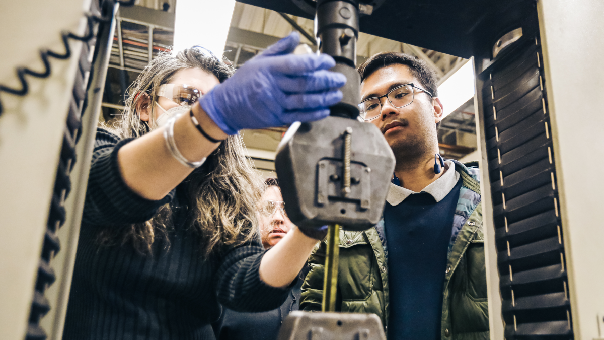 Two manufacturing students working on a machine with Dr. Yanika Schneider