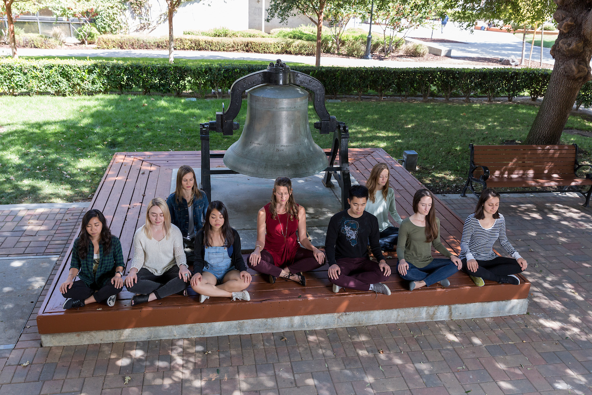 students meditating outside with a bell