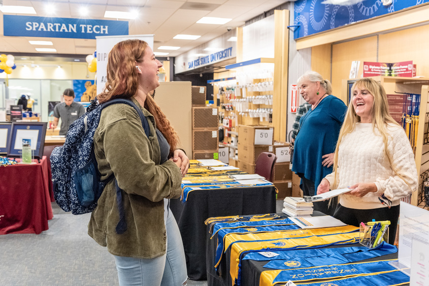 A student speaks with staff next to a table full of different stole styles.