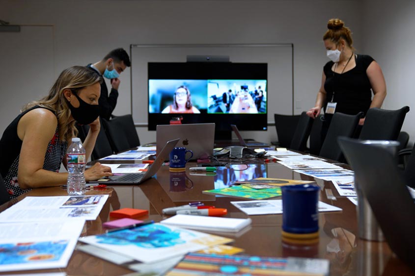 UMC employees working in a conference room with a zoom on the large screen showing a hybrid workspace.