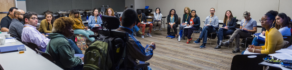 A group of approximately 30 people sitting on chairs in a circle while listening to the person in front speaking.