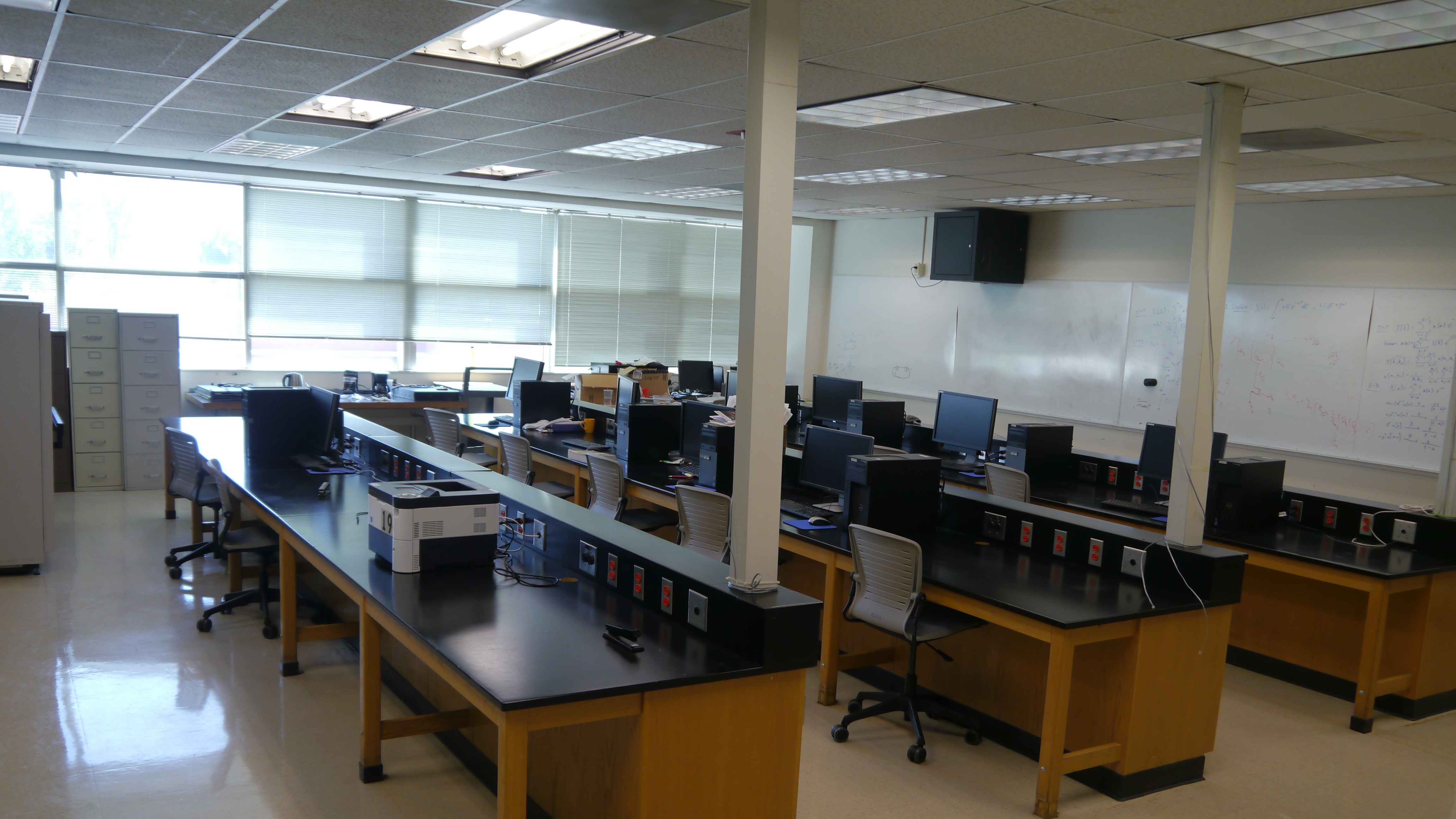 A dimly lit classroom with long tables and office chairs.