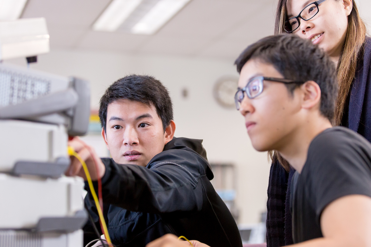 A student talks to his two peers as he points to a stack of electronic devices.