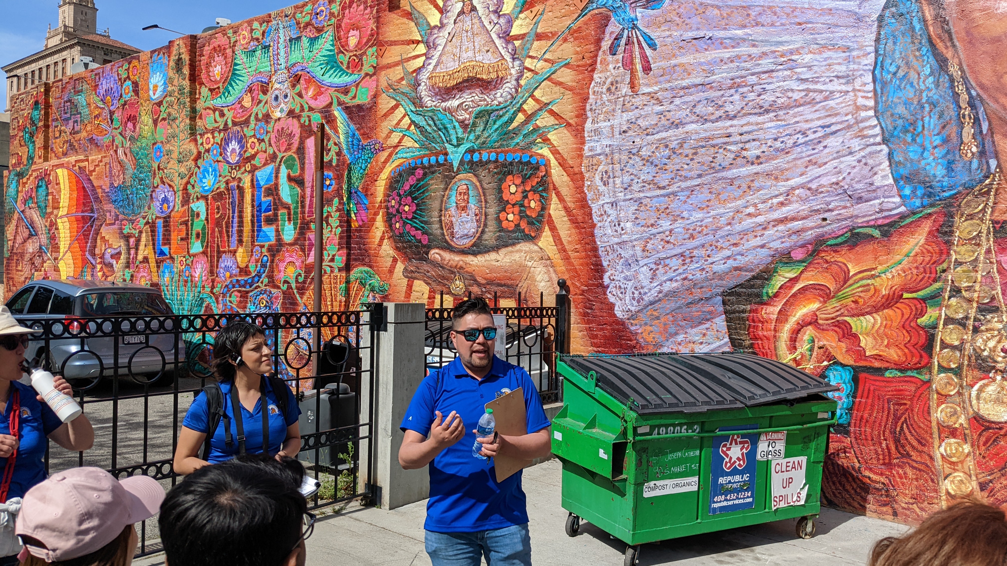 man standing in front of mural speaking to a group