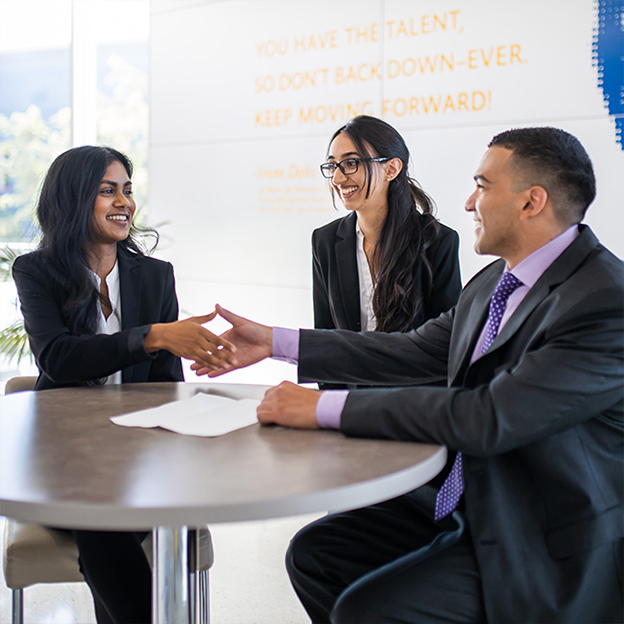 Three business people greeting each other around a small circular table.