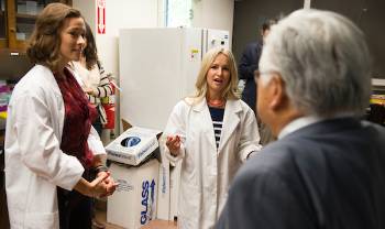 two people in lab coats explain something to a visitor in a suit