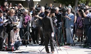 person stands outside ready to make a statement with a ton of video cameras and reporters around