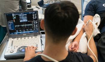 looking over a person's shoulder as they hold a sensor to a subject's arm and look at a readout on screen