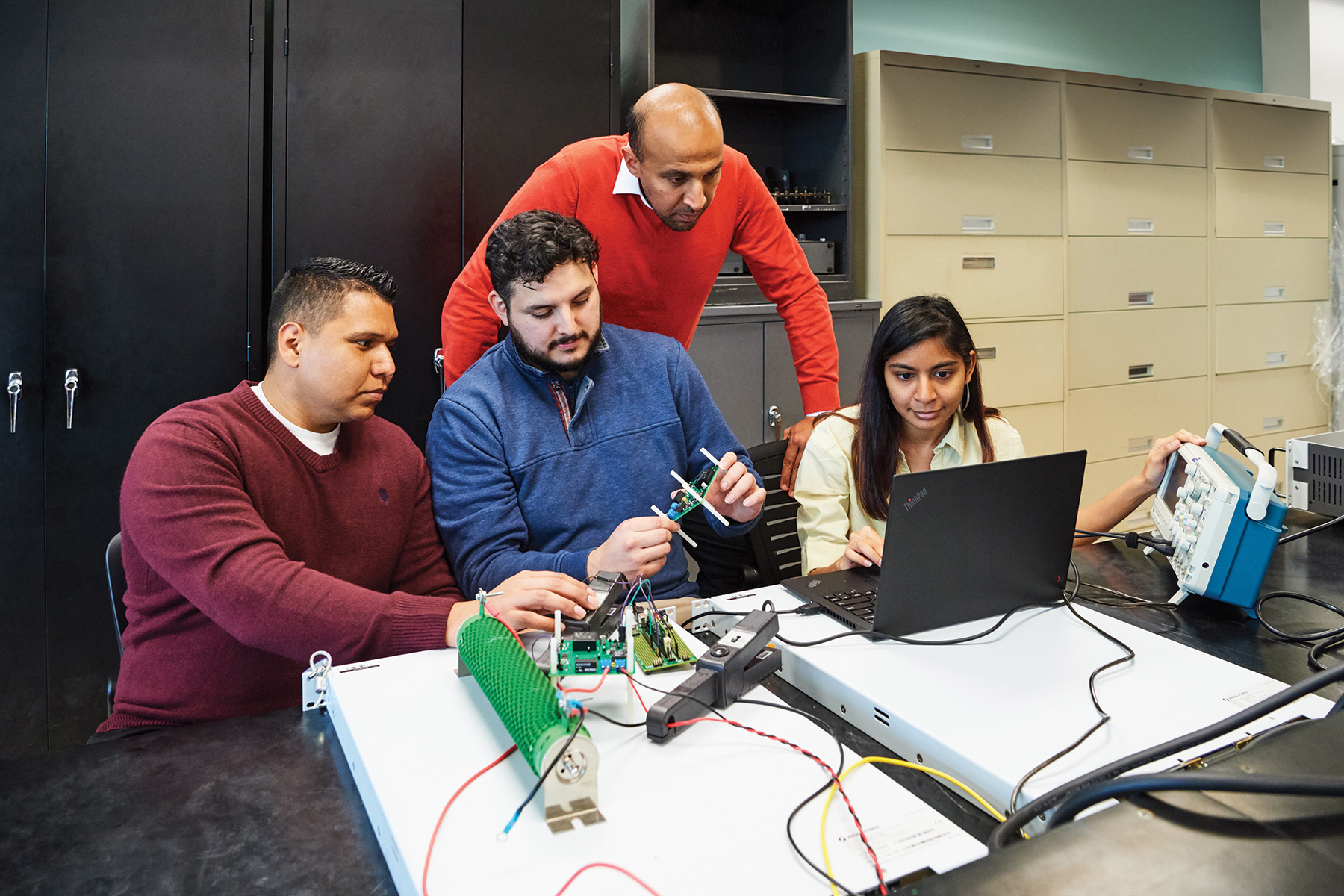 professor with three students at table with electrical equipment